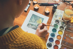 Person painting a picture of a forest with watercolors.